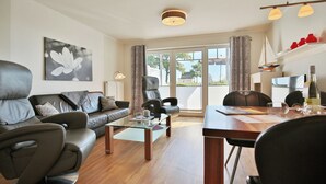 A modern living room with a leather sofa, a glass coffee table, and a dining area with a wooden table and chairs. - Strandvilla Appartement 3 (Scharbeutz)