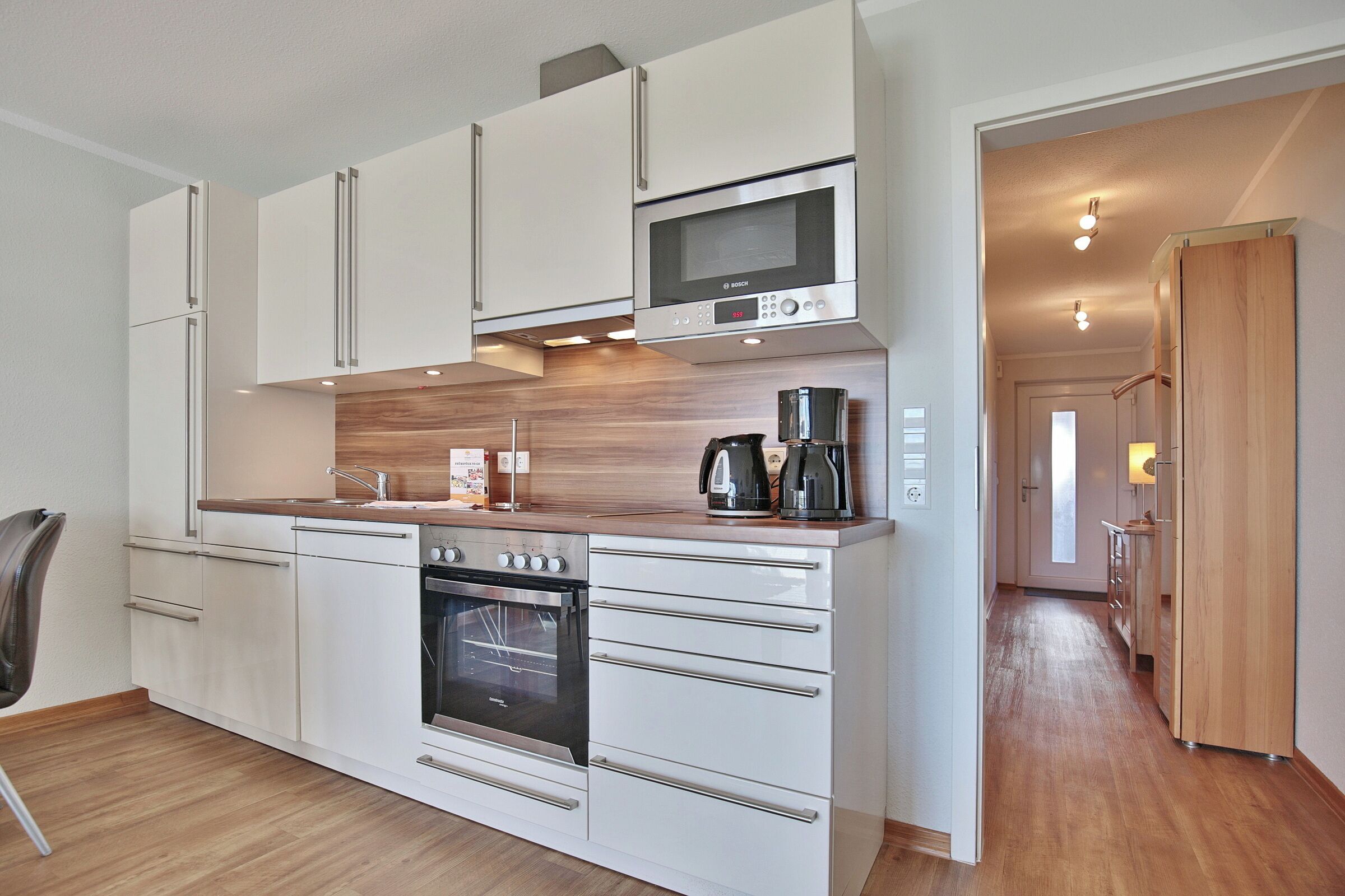 A modern kitchen with white cabinetry, a Bosch microwave, a coffee maker, and a built-in oven.