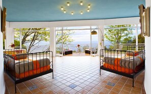 A sunlit room with two metal-framed beds, a tiled floor, and large windows offering a view of the sea. - 4 Bedroom villa with private pool and sea views in Amalfi Coast (Piano di Sorrento)