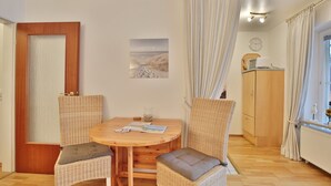 A room with a wooden table, two wicker chairs, a wooden cabinet, and a window with curtains. - Seepark Appartement 13 (Scharbeutz)