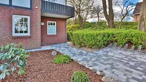 A two-story building with a brick facade, a balcony, and a paved walkway leading to the entrance. - Seepark Appartement 13 (Scharbeutz)