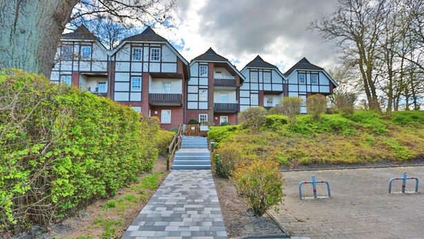 A row of traditional-style buildings with multiple balconies and a paved pathway leading to the entrance. - Seepark Appartement 13 (Scharbeutz)