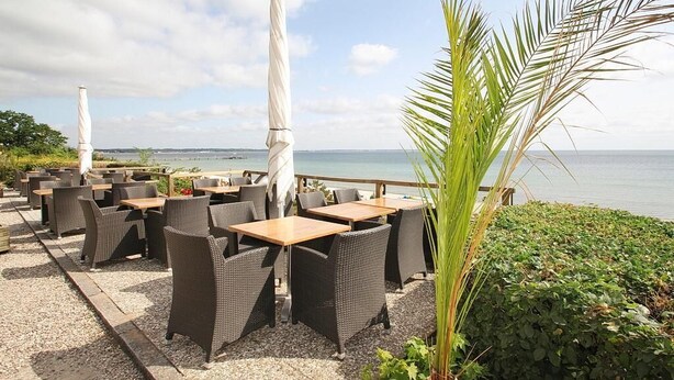 An outdoor seating area with wicker furniture and umbrellas, overlooking a body of water. - Residenz am Hang Appartement 103 (Scharbeutz)