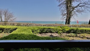 A view of a landscaped area with a body of water in the background, a red flag, and leafless trees. - Residenz am Hang Appartement 103 (Scharbeutz)