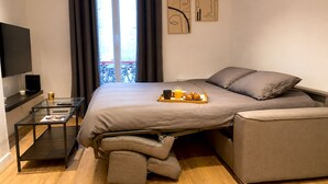 A modern bedroom with a bed, a TV, a glass table, and a balcony view.