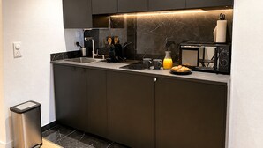 A modern kitchen with dark cabinetry, a marble backsplash, a built-in microwave, and a coffee maker.