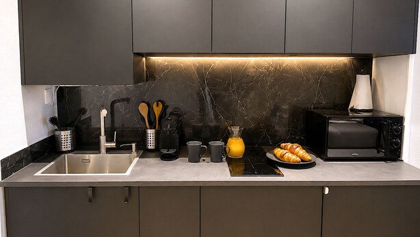 A modern kitchen with dark cabinets, a marble backsplash, a sink, a toaster, and a croissant plate.