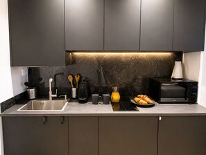 A modern kitchen with dark cabinets, a marble backsplash, a sink, a toaster, and a croissant plate. - Le Loft Levis (Paris)