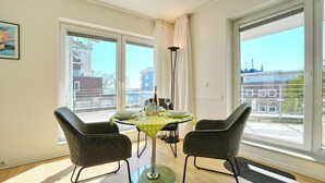 A dining area with a glass table, two chairs, a floor lamp, and large windows. - Barke Appartement 324 (Scharbeutz)