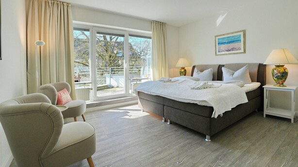 A bedroom with a bed, two bedside tables, a chair, a window with curtains, and a painting on the wall. - Barke Appartement 324 (Scharbeutz)
