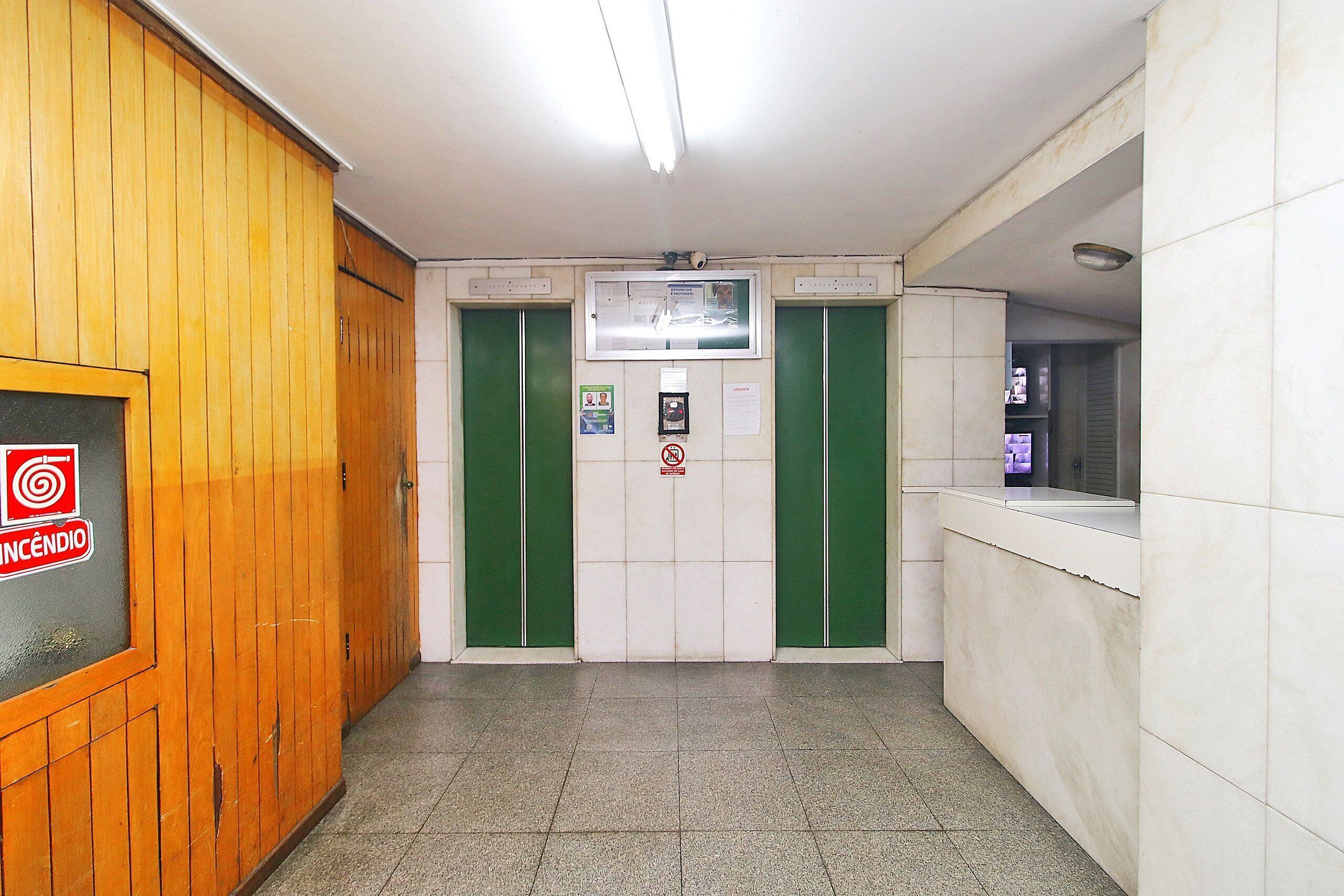Un pasillo con paneles de madera en una pared, puertas verdes y suelo de baldosas.