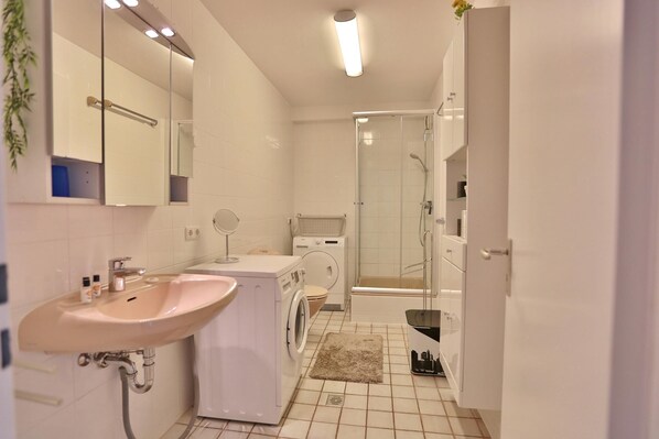 A modern bathroom with a sink, mirror, washing machine, and shower. - Strandläufer Appartement 2 (Scharbeutz)