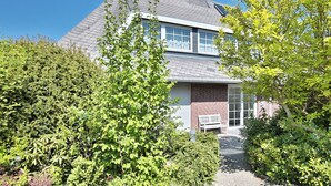 Ein zweistöckiges Haus mit Backsteinfassade, einem geneigten Dach und einer Veranda mit einer Bank.