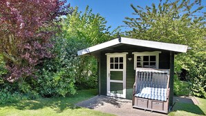 Ein kleines, eingeschossiges Gebäude mit Veranda und Sitzgelegenheit mit Kissen.