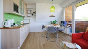 Een moderne keuken met houten kastjes, een zithoek met tafel en stoelen, een rode bank en een groot raam met uitzicht op de omgeving.