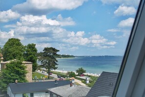 A coastal view from a window overlooking a beach, with a clear sky and a few clouds.