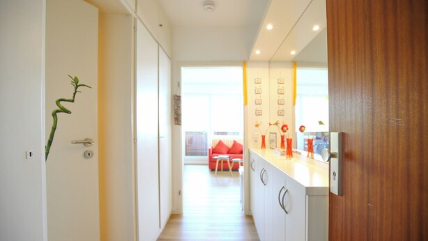 Een moderne keuken met witte kasten, een houten deur en uitzicht op een woonkamer met een rode bank.