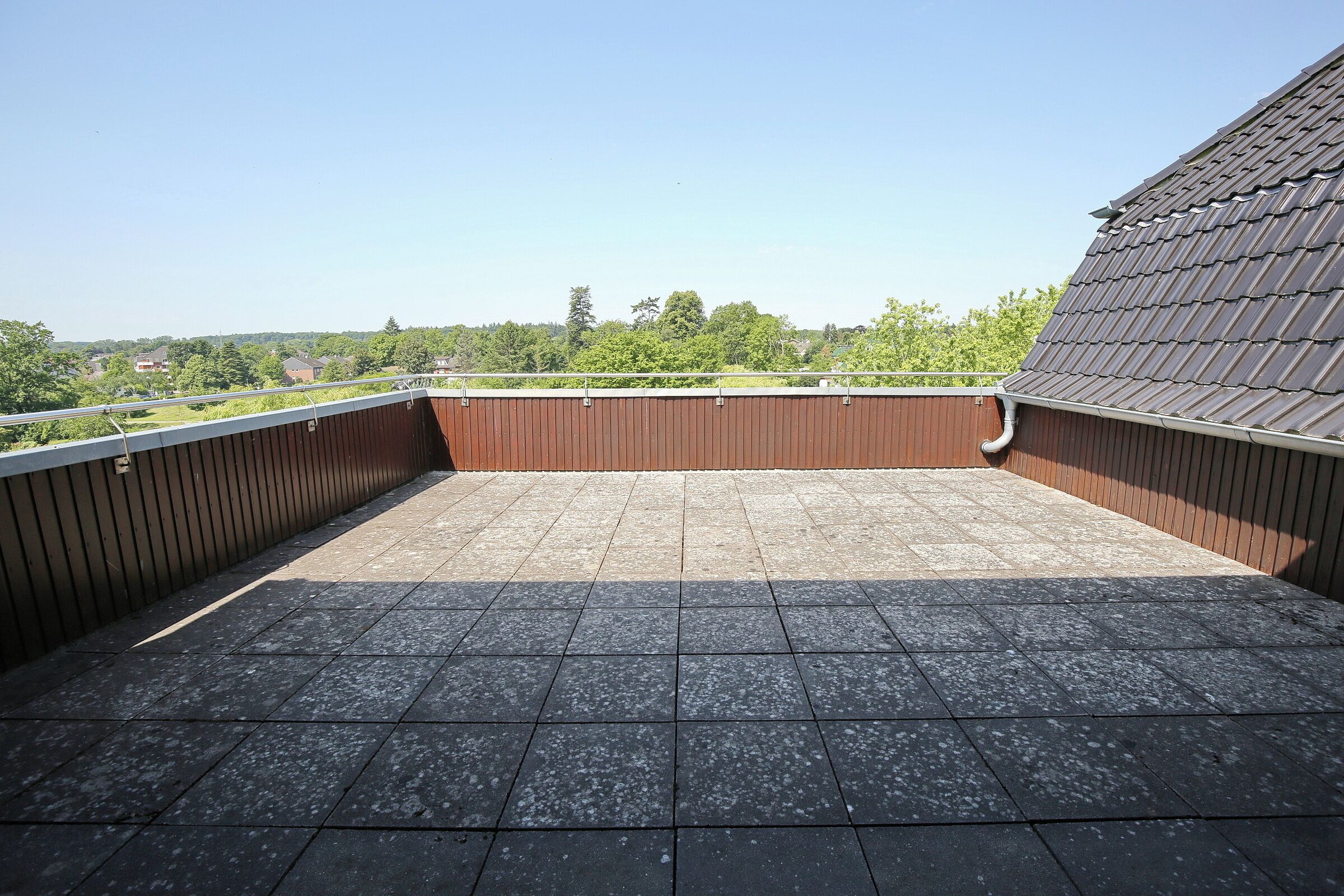 A rooftop terrace with a view of a green landscape and a clear sky.