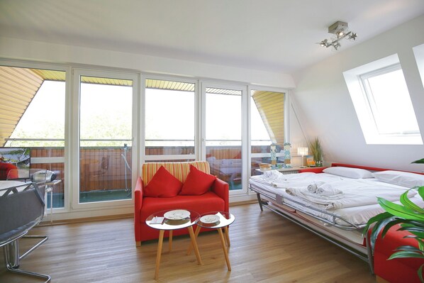 A modern room with a red sofa, a bed, a dining table, and large windows.