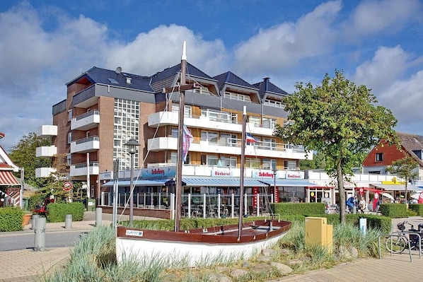 A multi-story building with balconies, a central courtyard, and storefronts with signage. - Perle de la Plage Apartment 403 (Haffkrug)