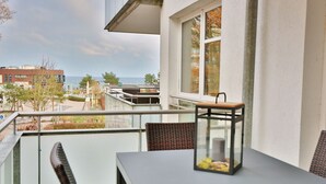 A balcony with a table and chairs, a lantern, and a view of the sea and buildings.