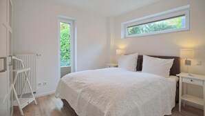 Un dormitorio con una cama grande, una ventana, un radiador y una mesita de noche con lámpara.