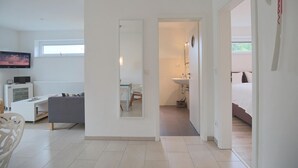 A modern living room with a TV, a sofa, and a dining area. A bathroom is visible through an open door, featuring a sink and a mirror. - Haus Küstenkinder Louis Appartement 2 (Scharbeutz)