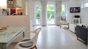 A modern living room with a dining area, a television, and a view through the glass doors. - Haus Küstenkinder Louis Appartement 2 (Scharbeutz)