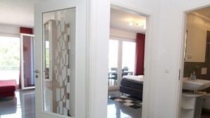 A modern hotel room with a glass door, a bed, a bathroom with a sink, and a view of the outdoors. - Strandglück Appartement 12B (Scharbeutz)