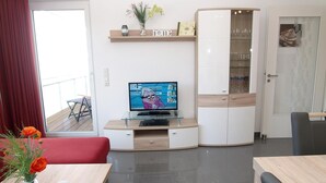 A modern living room with a flat-screen TV, a red sofa, a glass coffee table, and a dining area with a wooden table. - Strandglück Appartement 12B (Scharbeutz)