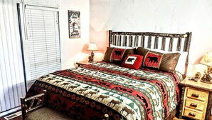 A bedroom with a bed, a nightstand, a chair, a window with blinds, and a wall with a poster. - Ski, Soak & Relax, 2 BR/1.5 BA Townhouse with Spa, at the base of Snow Summit (Big Bear Lake)