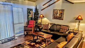 A cozy living room with a leather sofa, a wooden coffee table, and a patterned rug. There are two lamps on side tables, a red chair, and a Christmas tree. - Ski, Soak & Relax, 2 BR/1.5 BA Townhouse with Spa, at the base of Snow Summit (Big Bear Lake)