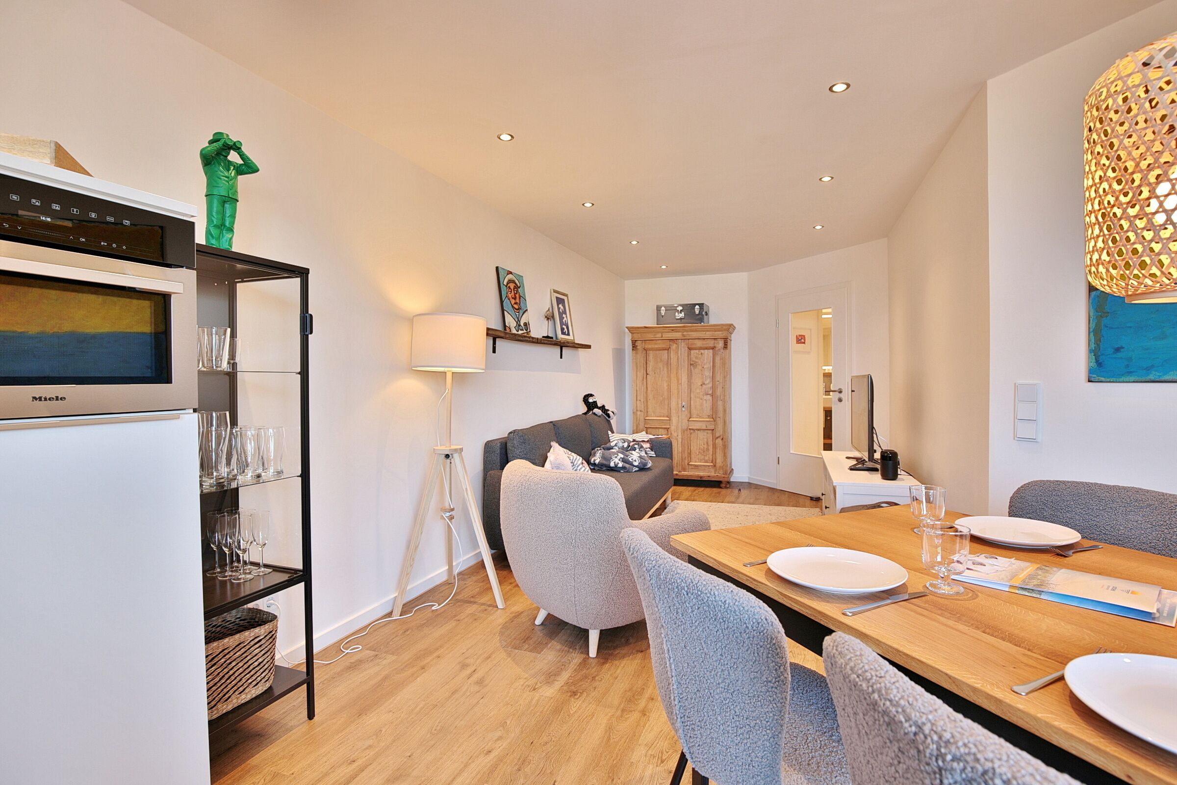 A modern kitchen with a built-in refrigerator, a dining table set for four, and a cozy seating area with a sofa and armchairs.