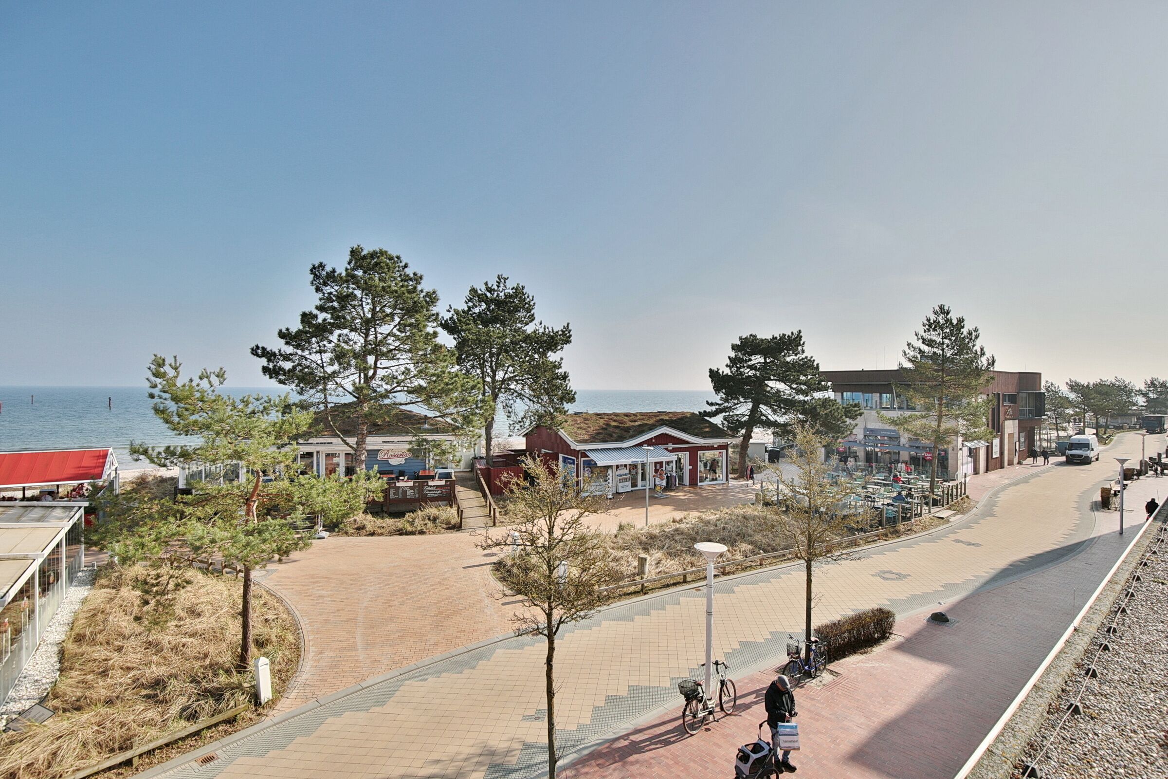 Une promenade en bord de mer avec un chemin pavé, des arbres et un bâtiment doté d’un toit rouge.