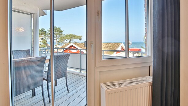 Ein Balkon mit Korbstühlen und Blick auf das Meer und die Gebäude.