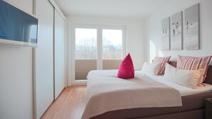 A bedroom with a bed, a TV mounted on the wall, and a window with blinds. - Strandglück Appartement 9B (Scharbeutz)