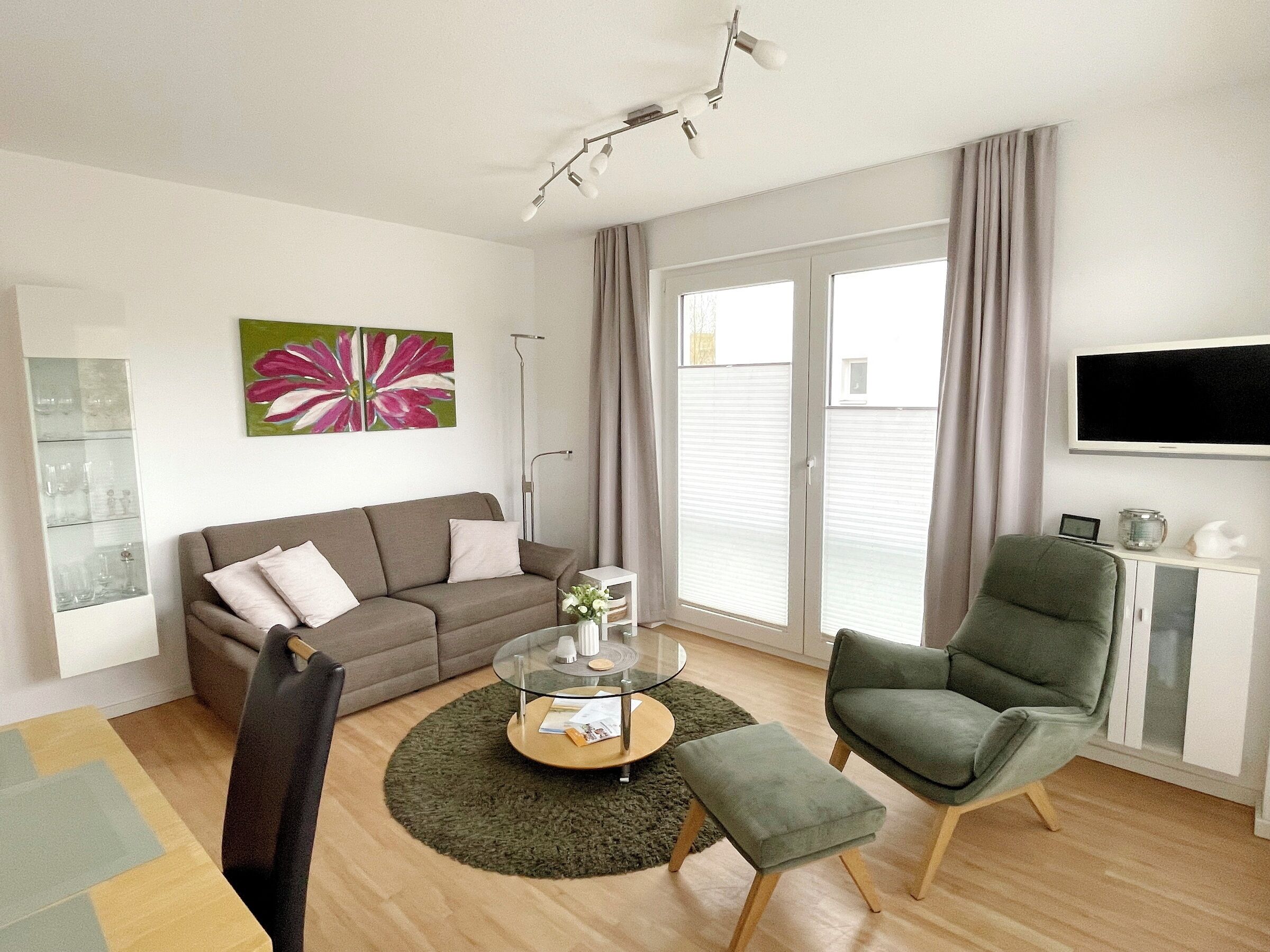 Ein modernes Wohnzimmer mit einer Couch, einem Glastisch, einem grünen Sessel und einem an der Wand montierten Flachbildfernseher.