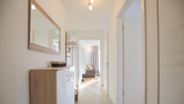 A hallway with a wooden cabinet, a mirror, and a door leading to a living area. - Strandglück Appartement 9B (Scharbeutz)