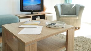 Una sala de estar con una mesa de centro de madera, un televisor de pantalla plana, un sillón azul claro y un tapete color beige.
