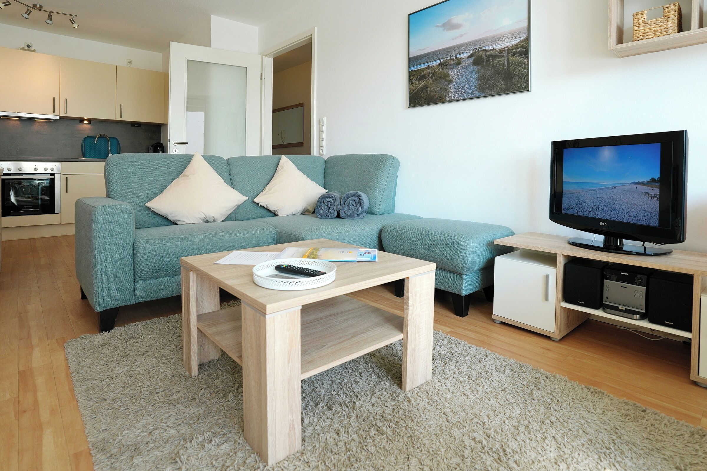 Een woonkamer met een bank, een salontafel, een televisie en een keuken op de achtergrond.