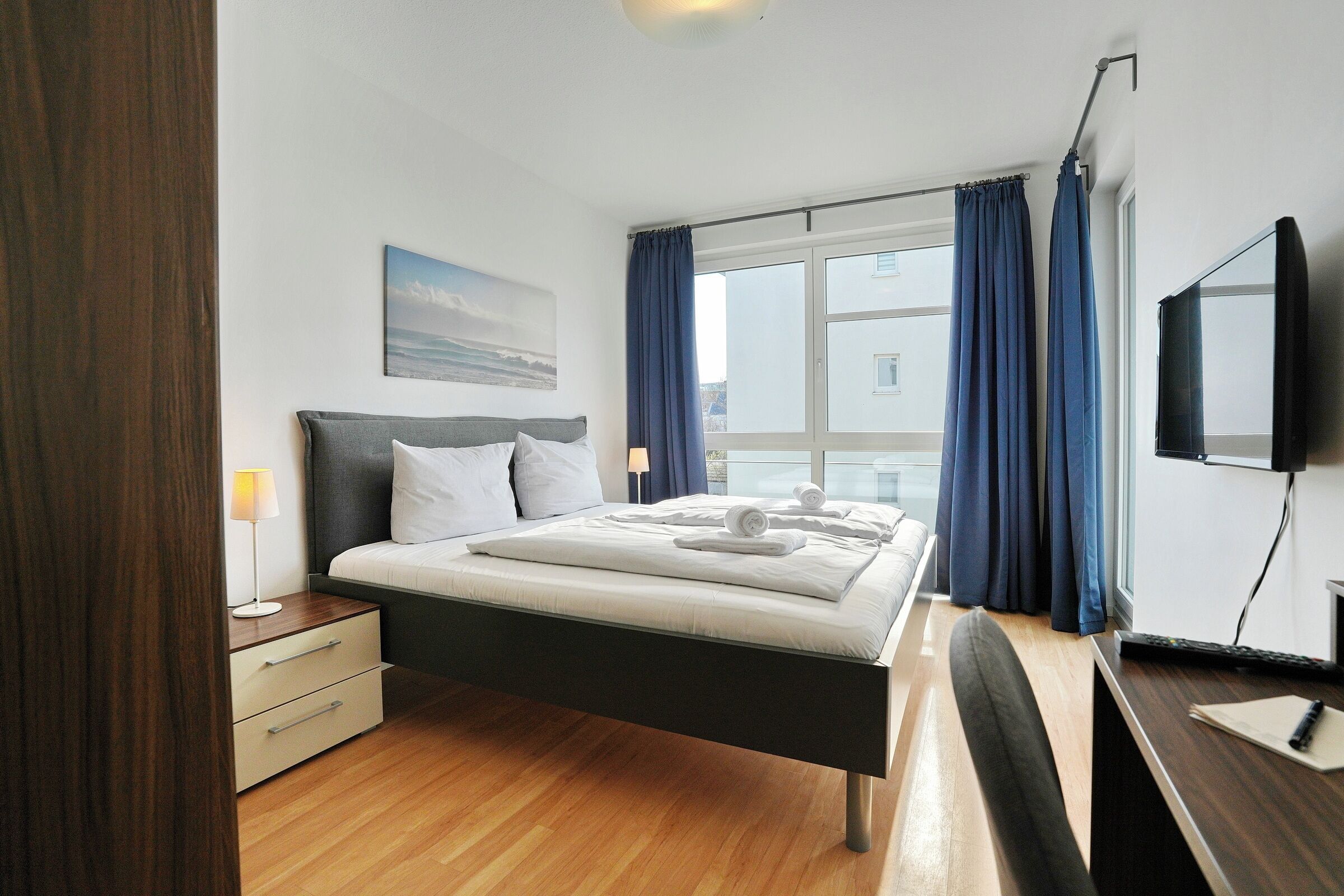 Ein modernes Hotelzimmer mit Bett, Nachttisch, Lampe und einem Flachbildfernseher.