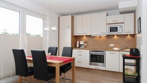 A modern kitchen with white cabinets, a wooden countertop, and a dining area with a red table and black chairs. - Strandglück Appartement 15C (Scharbeutz)