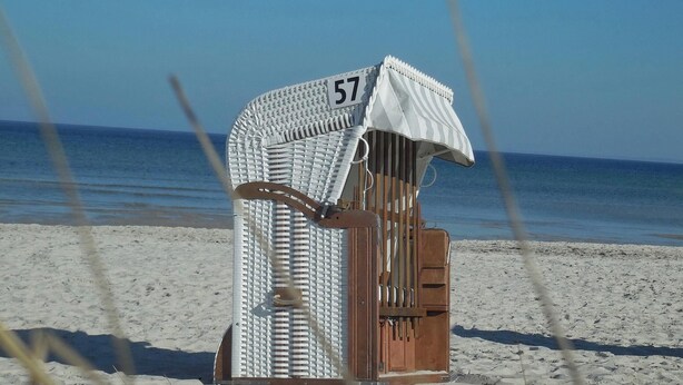 A beach chair with a striped cover and the number 57, placed on a sandy beach with the sea in the background. - Strandglück Appartement 15C (Scharbeutz)