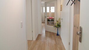 A hallway with a wooden floor, white walls, and a door leading to a room with a table and chairs. - Strandglück Appartement 15C (Scharbeutz)