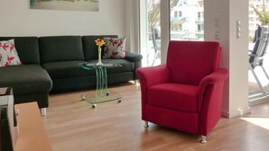 A modern living room with a dark green sofa, a red armchair, a glass coffee table, and a painting on the wall. - Strandglück Appartement 15C (Scharbeutz)