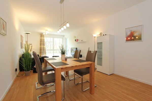 A modern dining area with a wooden table and chairs, a potted plant, and a white refrigerator. - Bonheur de Plage Apartment 13A (Scharbeutz)