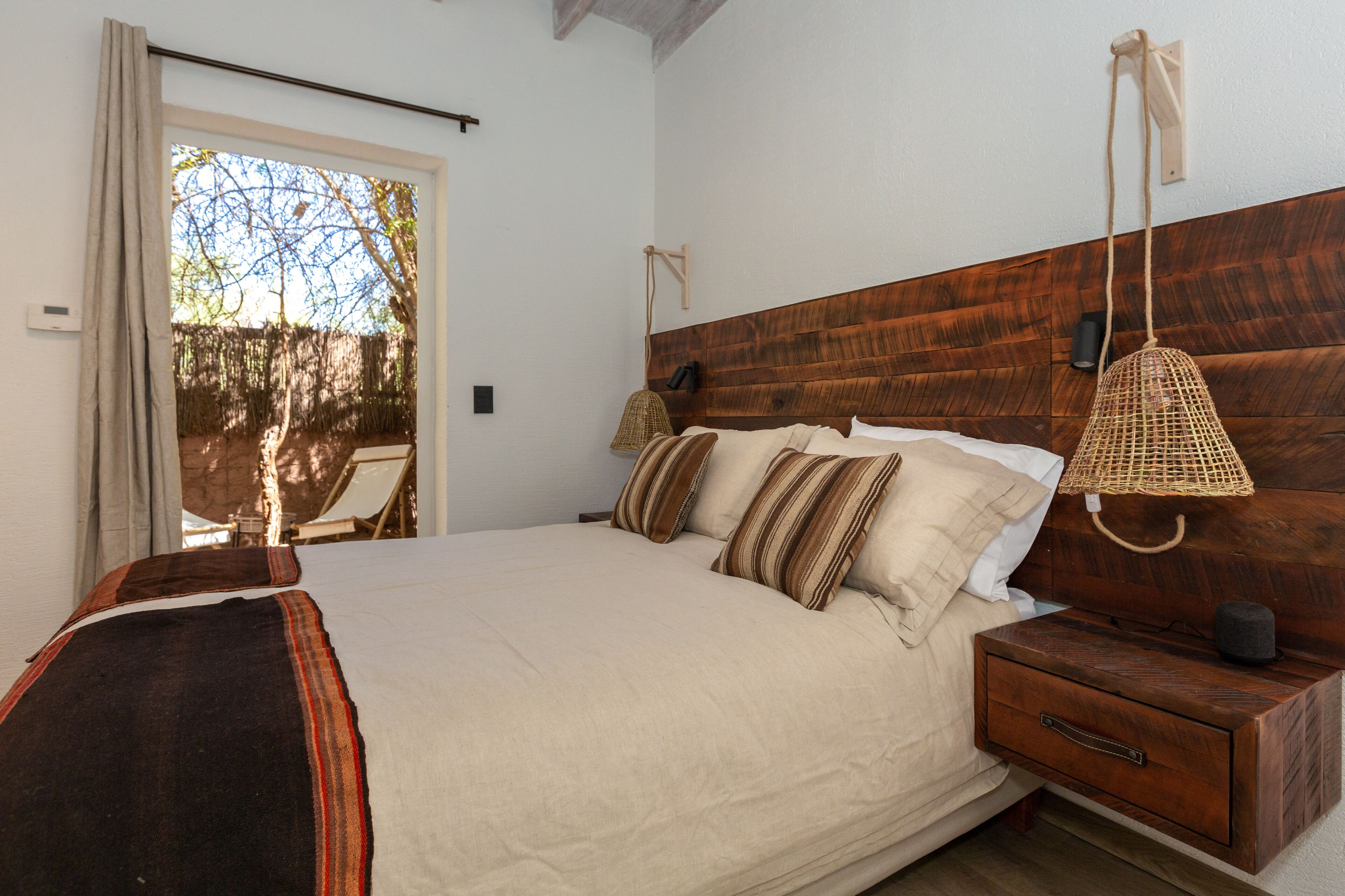 A bedroom with a large bed, wooden headboard, bedside lamps, and a view of the outdoors through a door.
