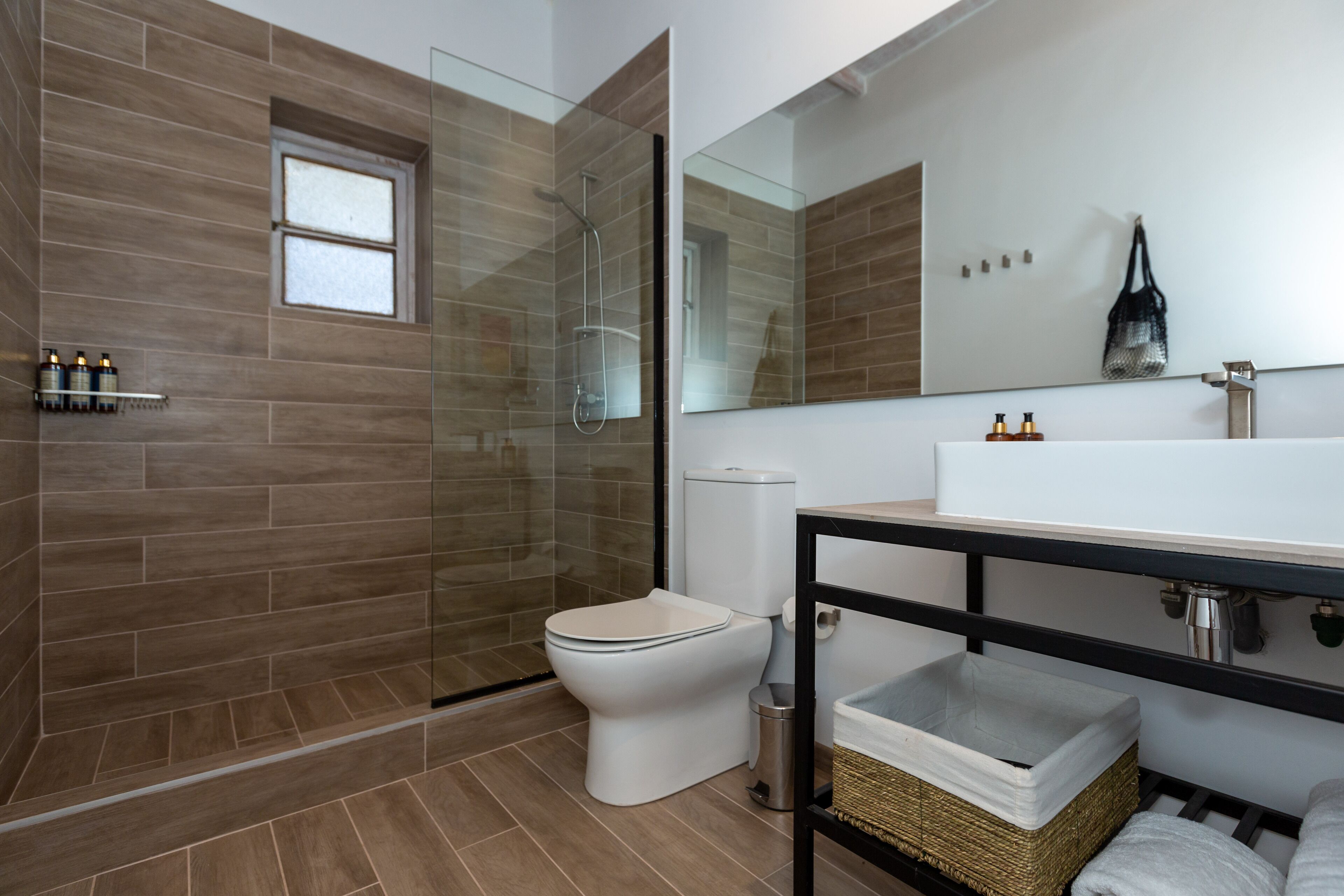 Ein modernes Badezimmer mit Duschkabine aus Glas, Toilette und großem Spiegel über einem Waschbecken.