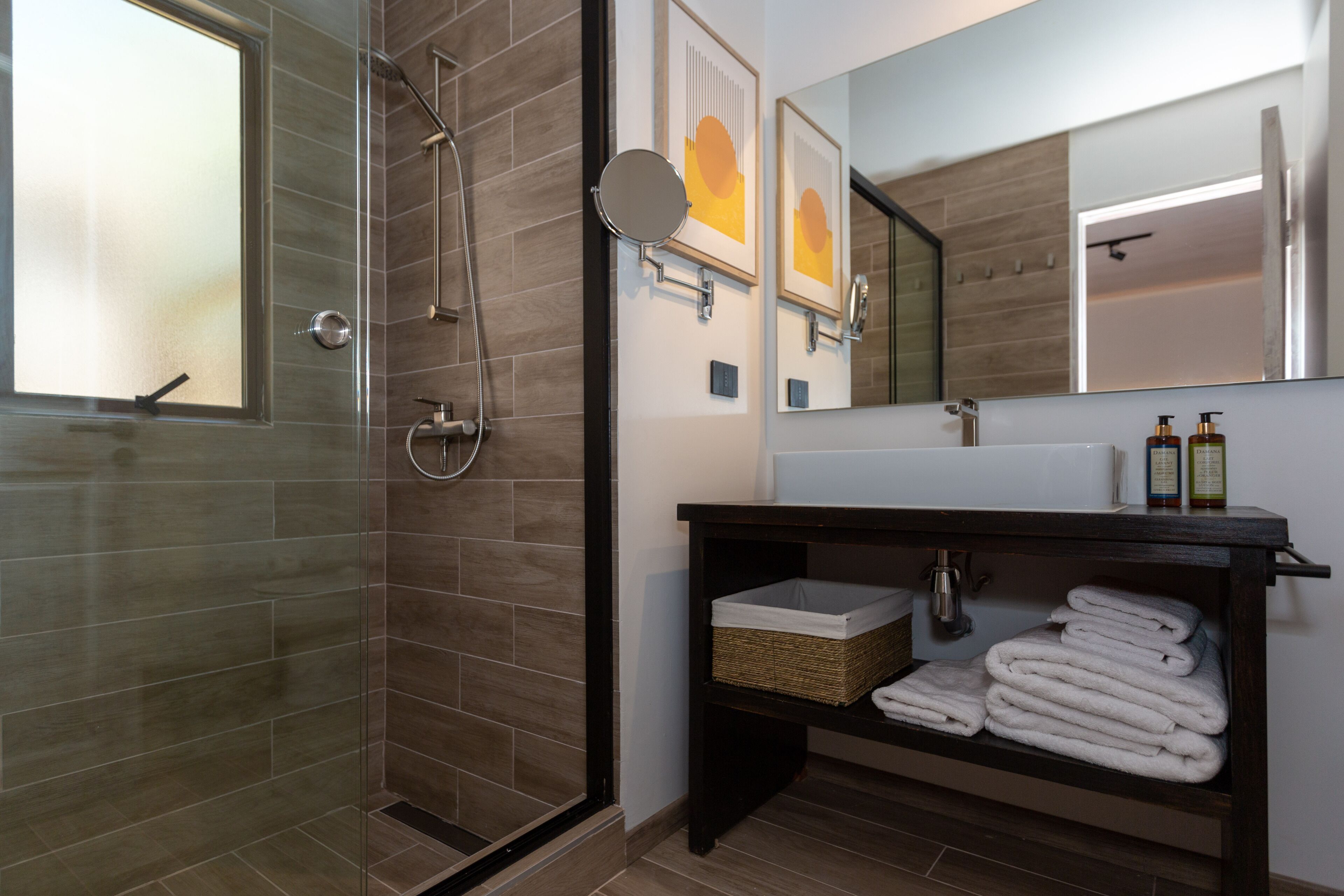 A modern bathroom with a glass-enclosed shower, a large mirror, and a vanity with towels and toiletries.