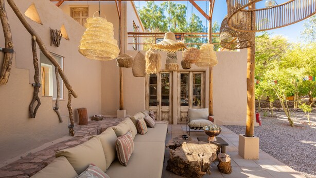 Un espacio al aire libre acogedor con un sofá, cojines y lámparas de mimbre colgantes.